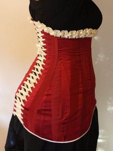 Side back of red striped satin 1911 long line corset with cream satin trimmings and cream satin laces