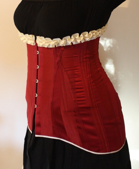 Side front of red striped satin 1911 long line corset with cream satin trimmings and cream satin laces